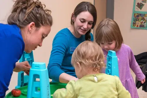 Two social work students playing in an indoor sandbox with two toddlers